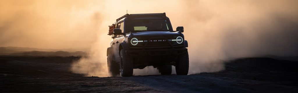 Ford Bronco off-roading in a dusty landscape at sunset.